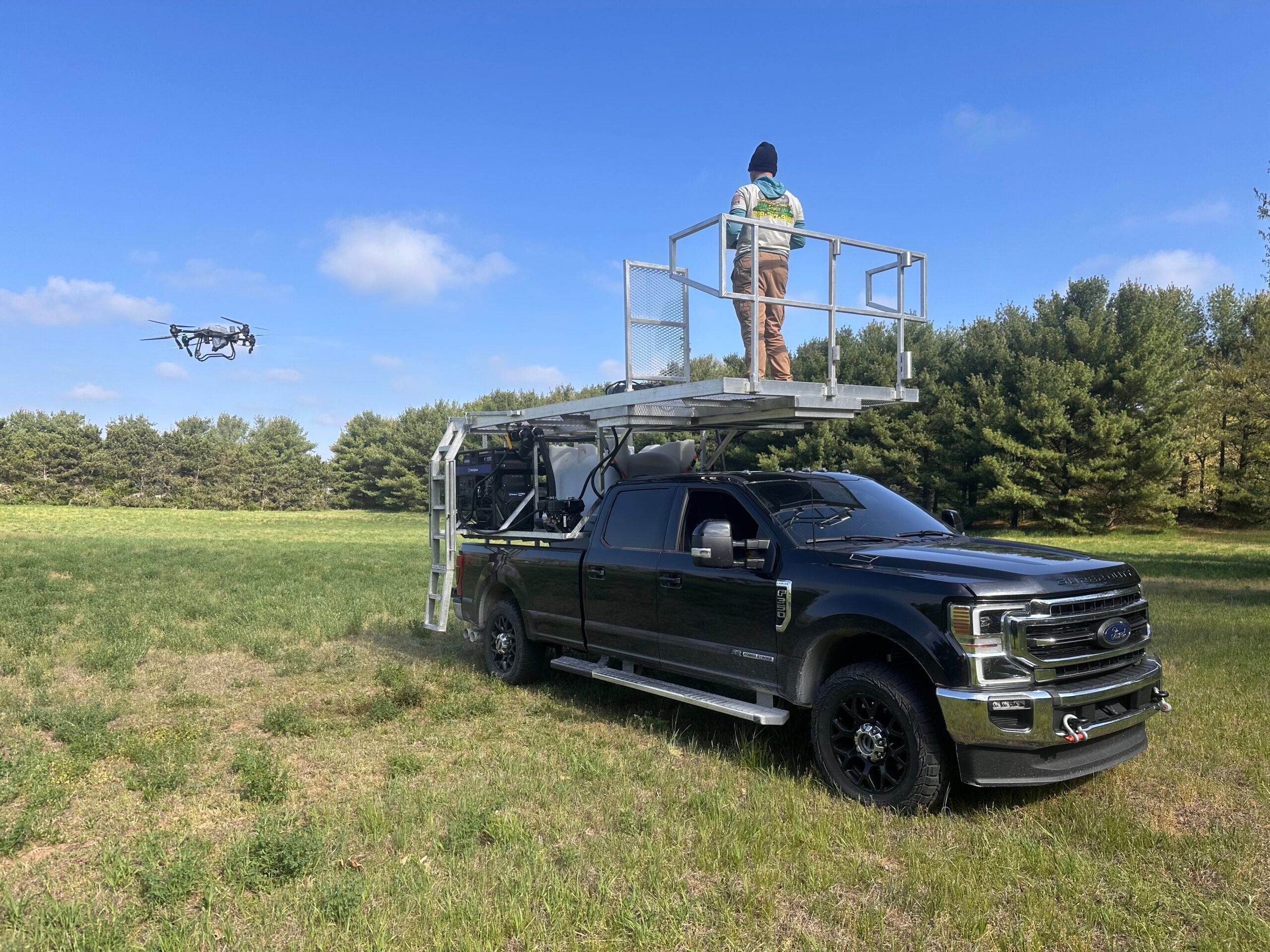 Heritage Drone Service pilot operating an agricultural drone from an elevated platform on a service truck during field operations. Heritage Drone Service pilot operating an agricultural drone from an elevated platform on a service truck during field operations.
