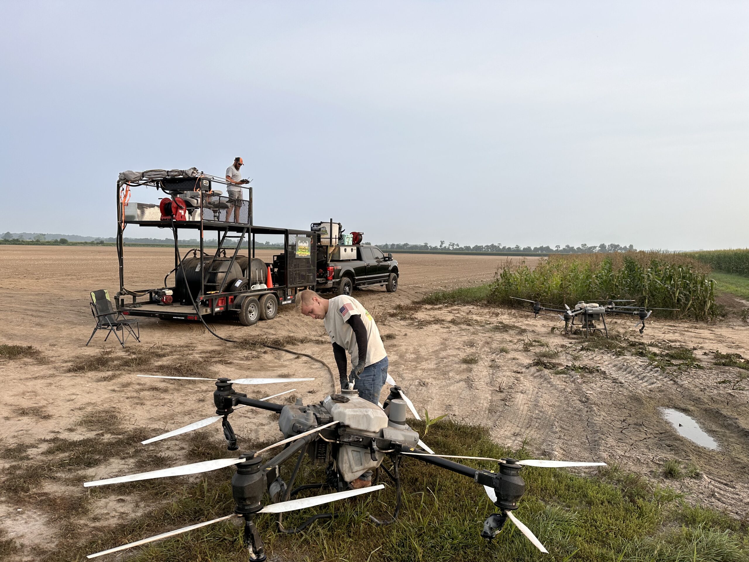 Heritage Drone Service crew preparing an agricultural drone for spraying operations with support trailer and equipment in the field.