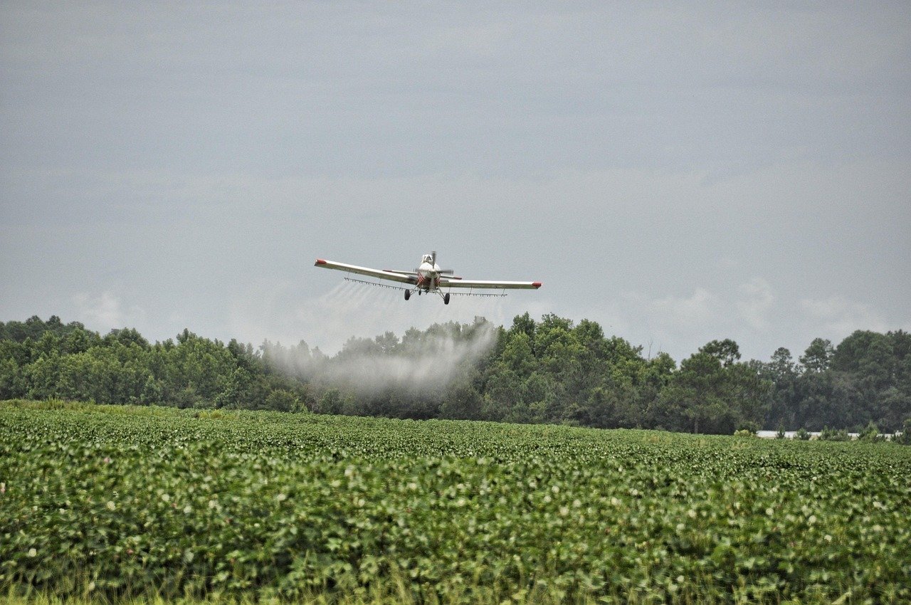 Crop dusting airplane applying chemicals over a field, illustrating traditional aerial application compared to modern drone spraying.irplane-465619_1280 Crop dusting airplane applying chemicals over a field, illustrating traditional aerial application compared to modern drone spraying.