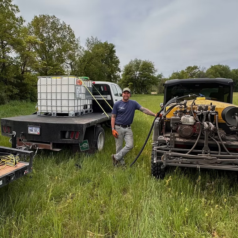 Heritage Drone Service technician standing beside spray mixing equipment and support vehicles in a field prior to drone application.
